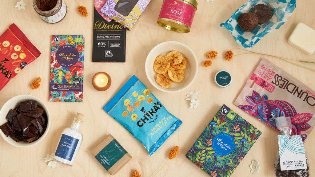 A selection of products from female-led businesses including Chika's, Chocolate and Love, Scintilla, Boundless Activated Snacking, Divine Chocolate, Cocoa Social Enterprise CIC, Refuge Chocolate and Grace Chocolates Changing Lives – all scattered randomly and shot from above.