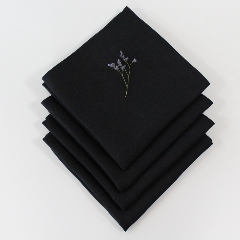 A stack of black Irish linen napkins with a piece of lavender on top.