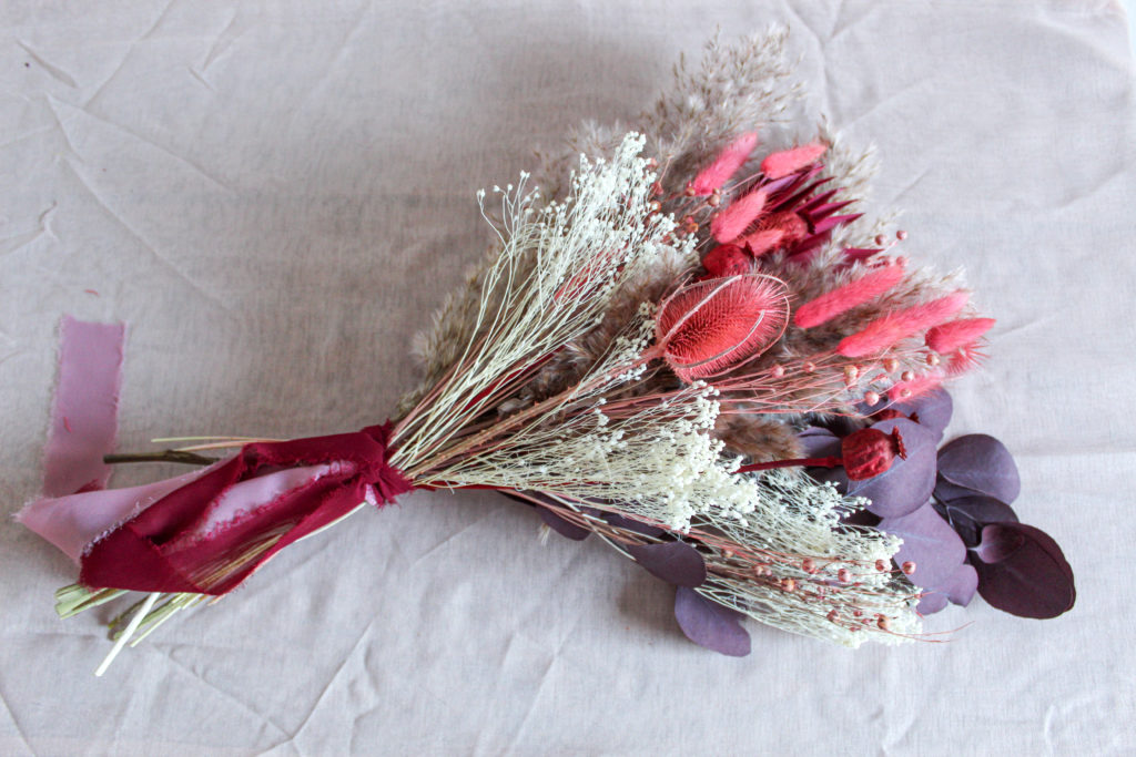 A bunch of dried flowers in shades of pink and purple by Strength & Stem on a linen table cloth