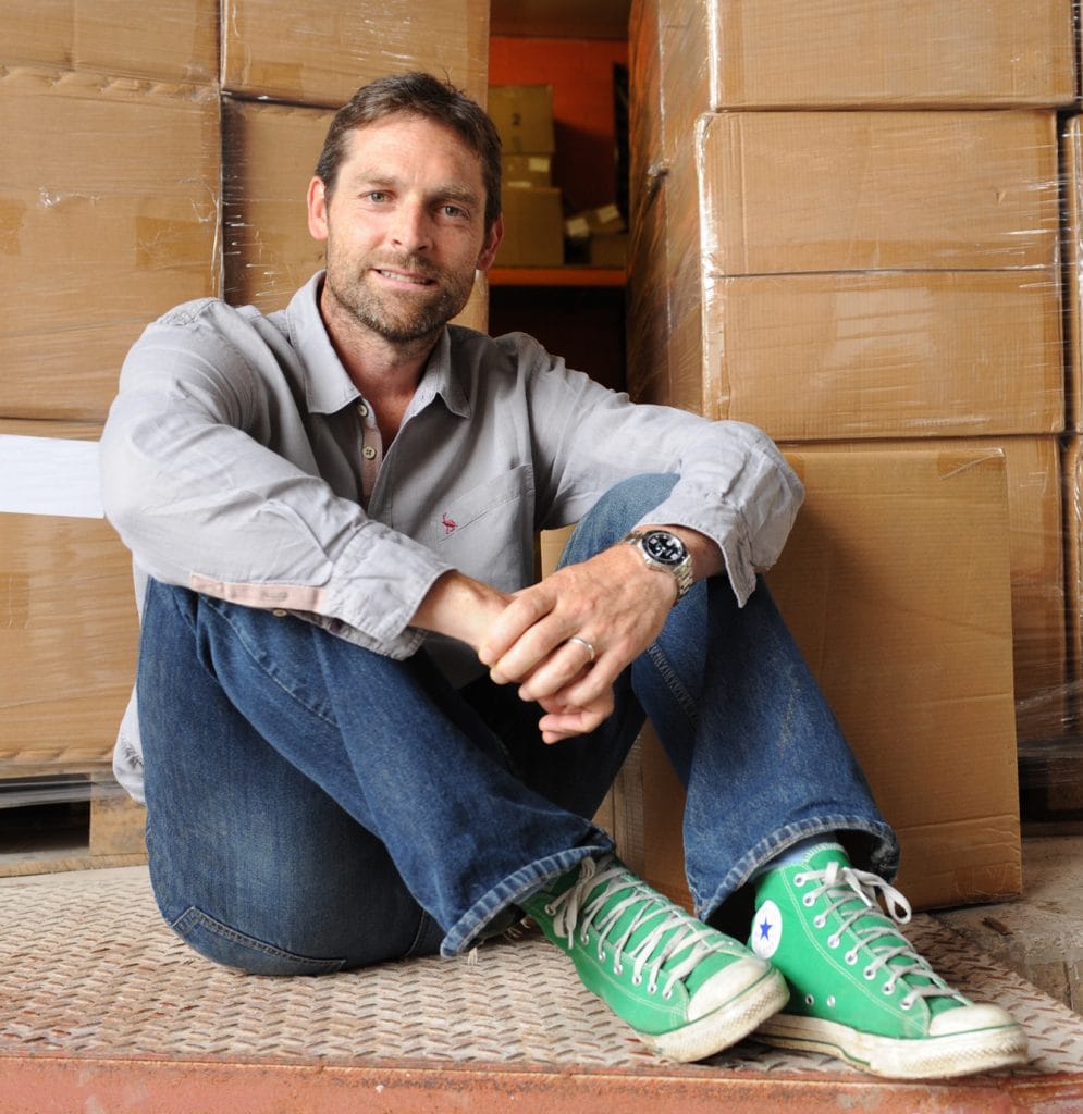 Evan, founder of VENT For Change, sits on the floor with his arms around his knees and boxes packed in the background.