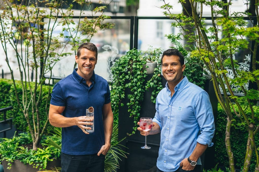 The co-founders of Served, Dean and Ryan, holding a drink each next to plants