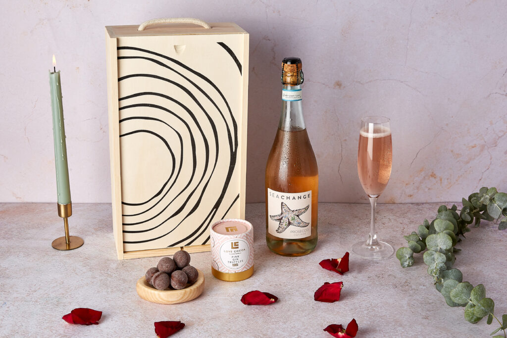 A bottle of Prosecco Rosé with gin truffles next to the wooden wine box they come in.