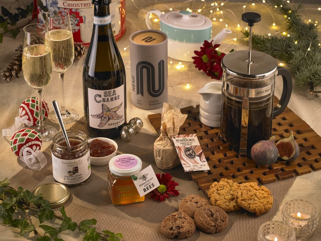 A Christmas breakfast table showing Prosecco, coffee in a French press, a selection of biscuits, honey, jam, figs and Christmas lights and foliage