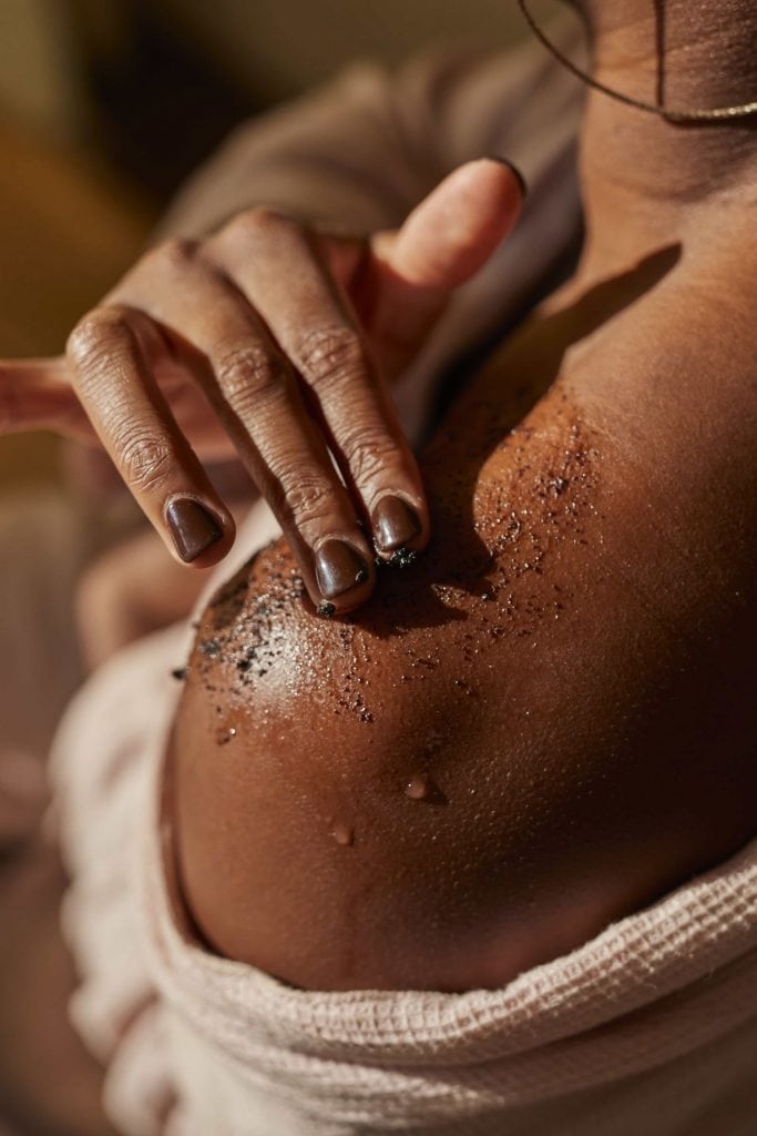 A close-up shot of a woman's shoulder; she's rubbing a body scrub into it with her opposite hand.