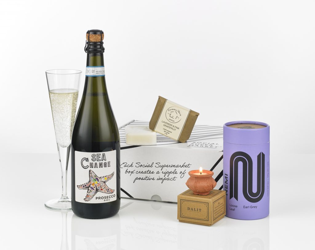 A gift box with its contents shown around it including a bottle of Prosecco, tea from NEMI Teas, a soap and a candle