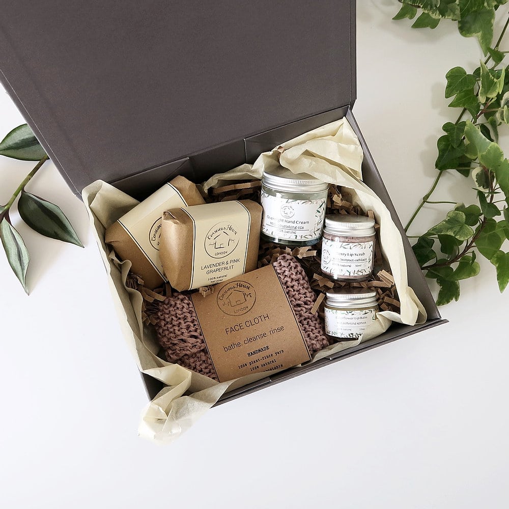 A gift box shot from a bird's eye view open showing its contents of beauty products and a hand knitted face cloth