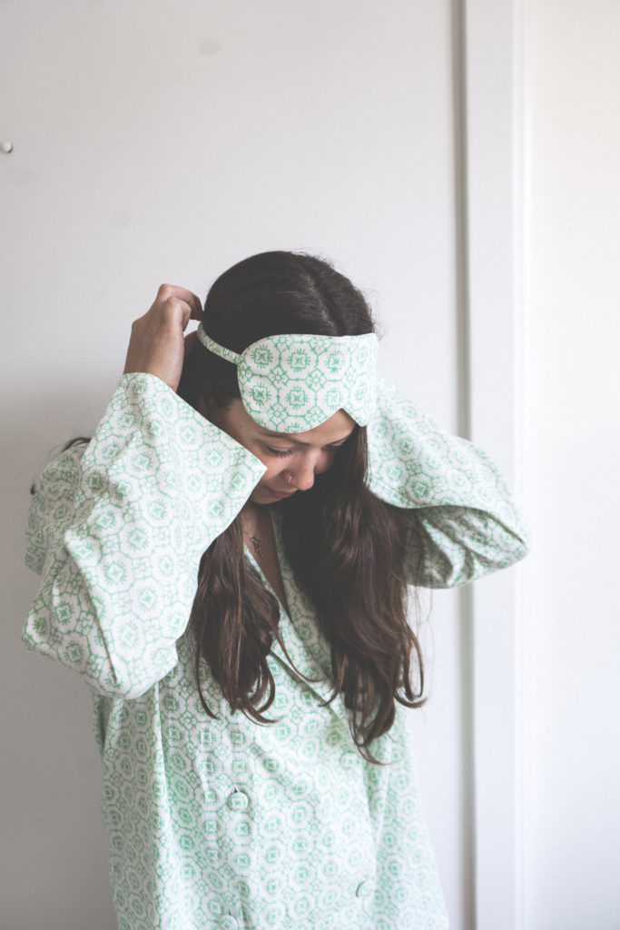 A model wearing the matching pyjamas puts on a Valerie eye mask in green tile over her forehead