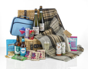 The Celebration picnic hamper open with its contents around it including two bottles of prosecco, a cool bag, a picnic blanket and drinks and snacks