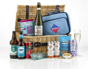 A picnic hamper showing its content including prosecco, a cool bag and a number of food and drink items