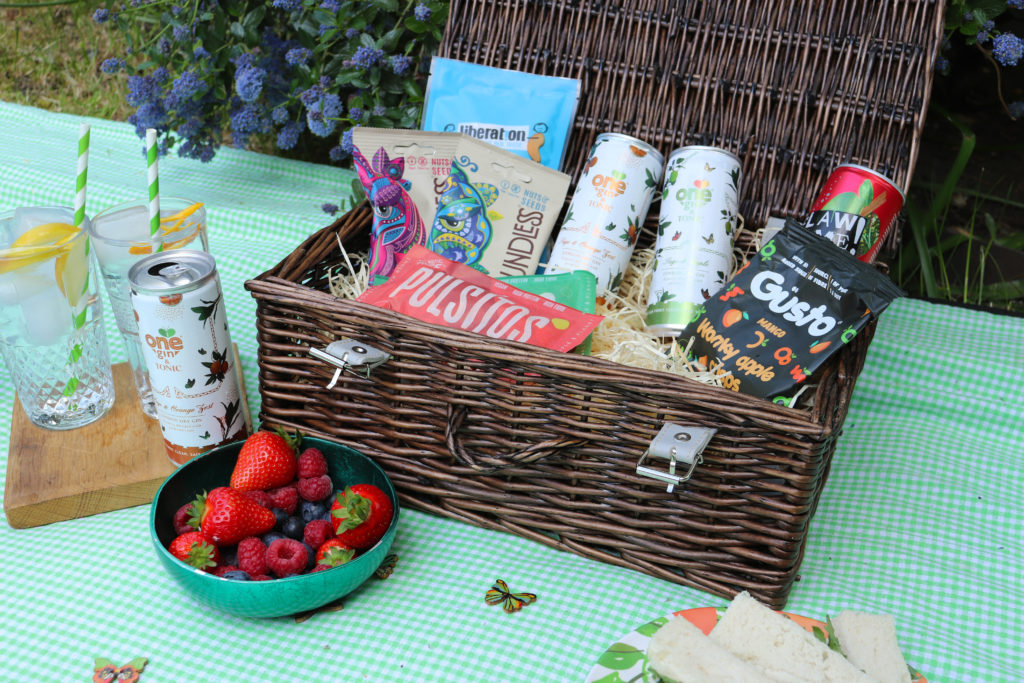 A Social Supermarket picnic hamper with One Gin cans plus snacks and other drinks, as well as strawberries in front of it