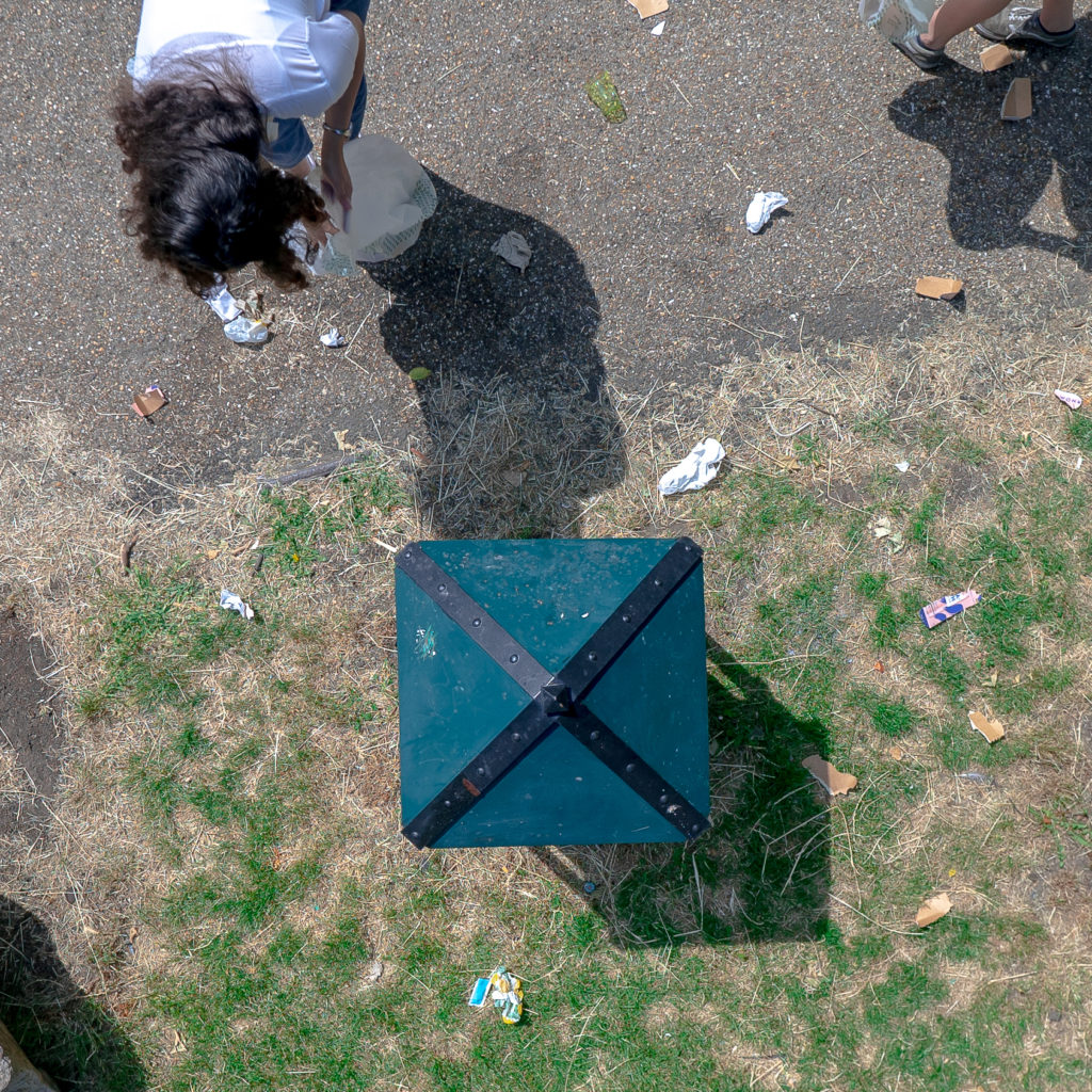 A woman shot overhead, bird's eye view collects litter next to a park bin