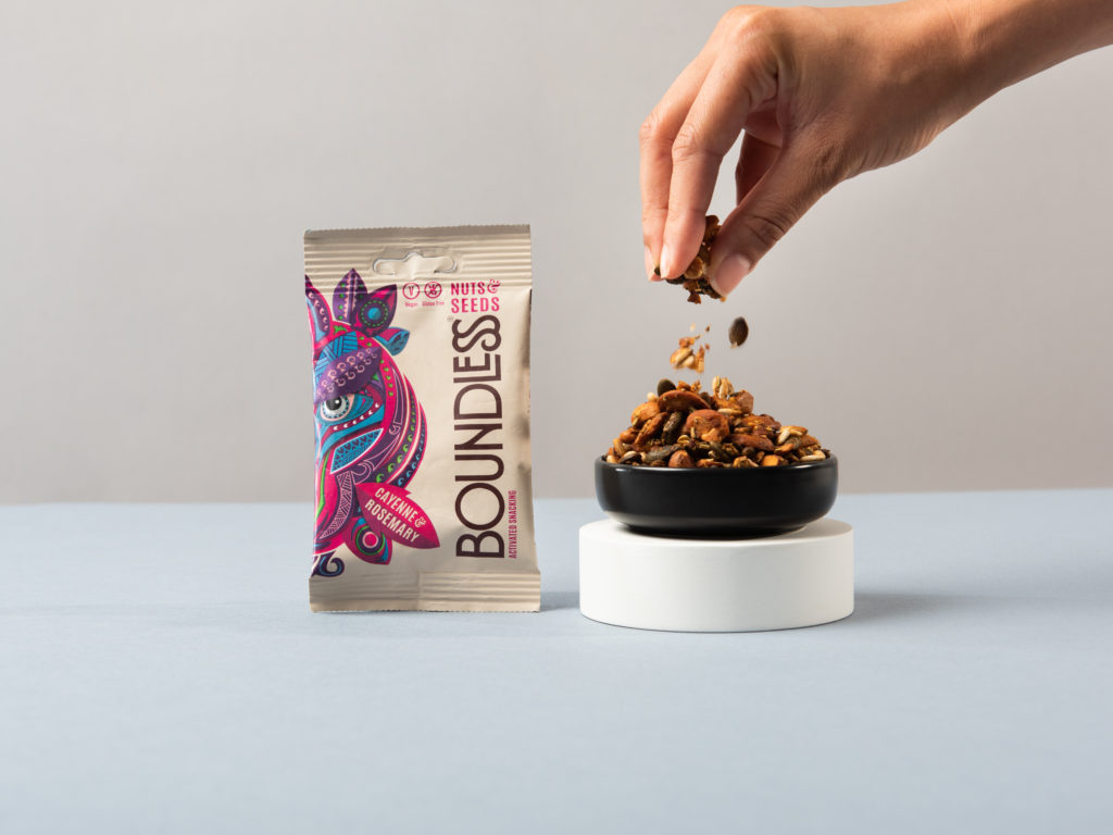 A bag of Boundless Activated Snacking nut mix next to an action shot of a hand picking up some nuts.