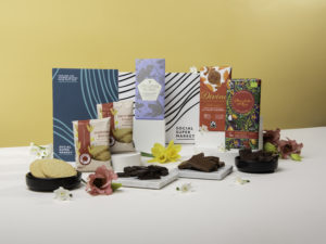 The Social Enterprise Chocolate Taster shown with its contents around the letterbox they come in, including chocolate bars from Original Beans, Chocolate and Love and Divine, and shortbread biscuits from Traidcraft