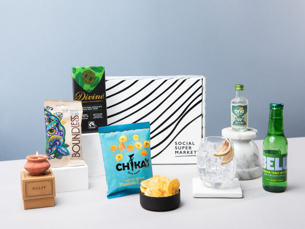 The Gin & Tonic gift box with its contents around it including a mini One Gin, a Belu tonic, Chikas and Boundless snacks, a Divine G&T chocolate bar and a Dalit mini candle.