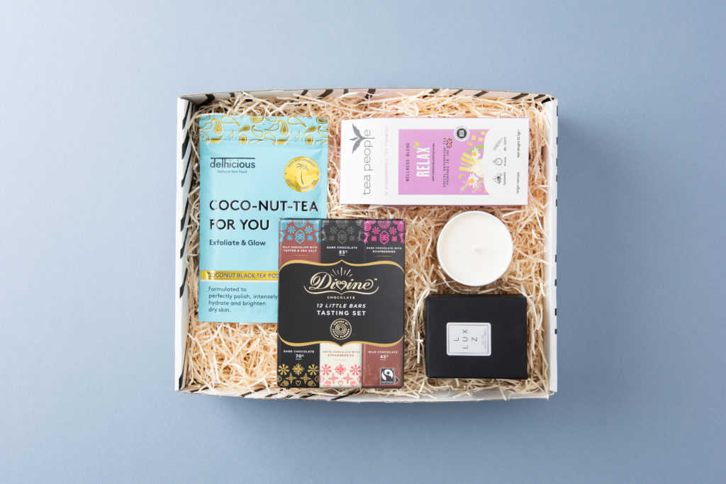 The Me-Time gift box shot from above with its contents inside including Tea People tea, Delicious Body body scrub, a LUX LUZ candle and a Divine Chocolate tasting set.