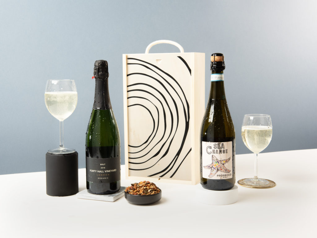 A display of 2 sparking wines, surrounded a wooden gift box