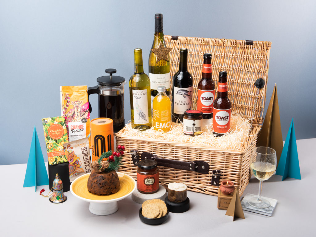 The Sweet Chestnut hamper by Social Supermarket with its contents in and around it including a Roots & Wings Organic Christmas pudding, NEMI Teas spicy chai, Toast Ale beers, Sea Change wine and Change Please coffee.