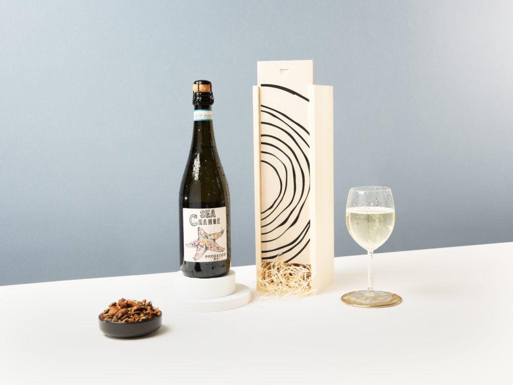 The Planet-Friendly Prosecco displayed against its wooden box and next to a bowl of nuts.