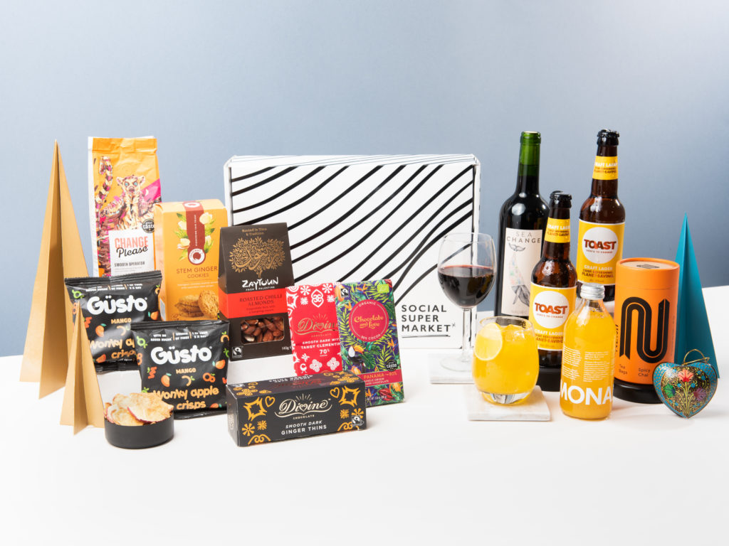 The Red Berry Rowan Christmas Gift Box by Social Supermarket showing its contents around it including wine by Sea Change, beer by Toast Ale and snacks by Güsto, among others.