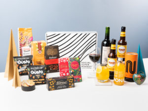 The Thinking of You Morale Booster Gift Box by Social Supermarket showing its contents around it including wine by Sea Change, beer by Toast Ale and snacks by Güsto, among others.