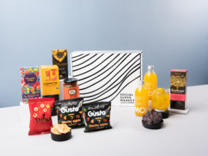 The Rest & Recuperate Gift Box is shown with its contents surrounding the box they all come in, including snacks from Güsto and Chika's, Traidcraft biscuits, Lemonaid drinks and Zaytoun dates, among others.