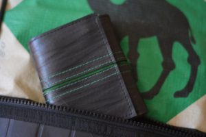 A green and black wallet displayed on a green animated camel bag.