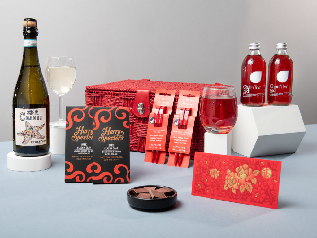 The Chinese New Year Hamper, including the red rope basket and its contents around it including Sea Chang Prosecco, Harry Specters chocolates, VENT For Change pens, ChariTea drinks and a red envelope.
