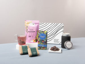 The Relax to the Max Wellbeing or Mother's Day Day Letterbox Gift surrounded by its contents including relax tea from Tea People chocolate from Chocolate and Love, a LUX LUZ Letterbox candle and two Scintilla soaps