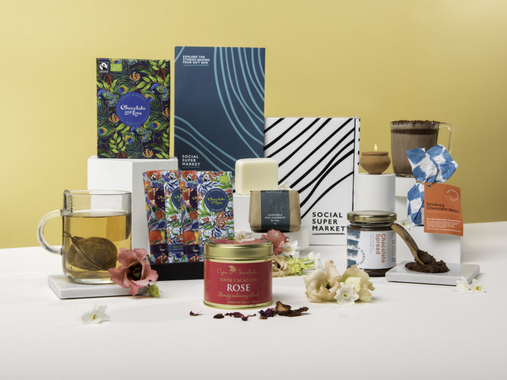 The International Women's Day Gift Box, with its contents surrounding the box they all come in, including Cocoa Social Enterprise Cacao Tea, a Chocolate and Love gift set, Refuge Chocolate spread and melts, a Dalit candle and a bar of Scintilla soap.
