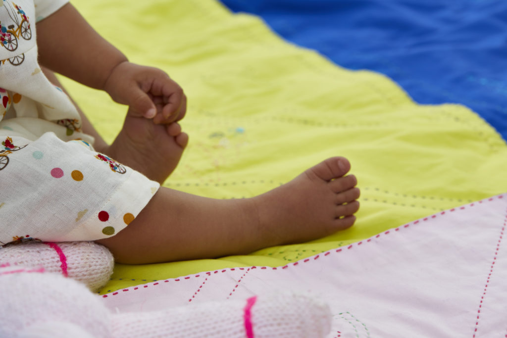 A child sits on a Khushi Kantha blanket and holds one toe