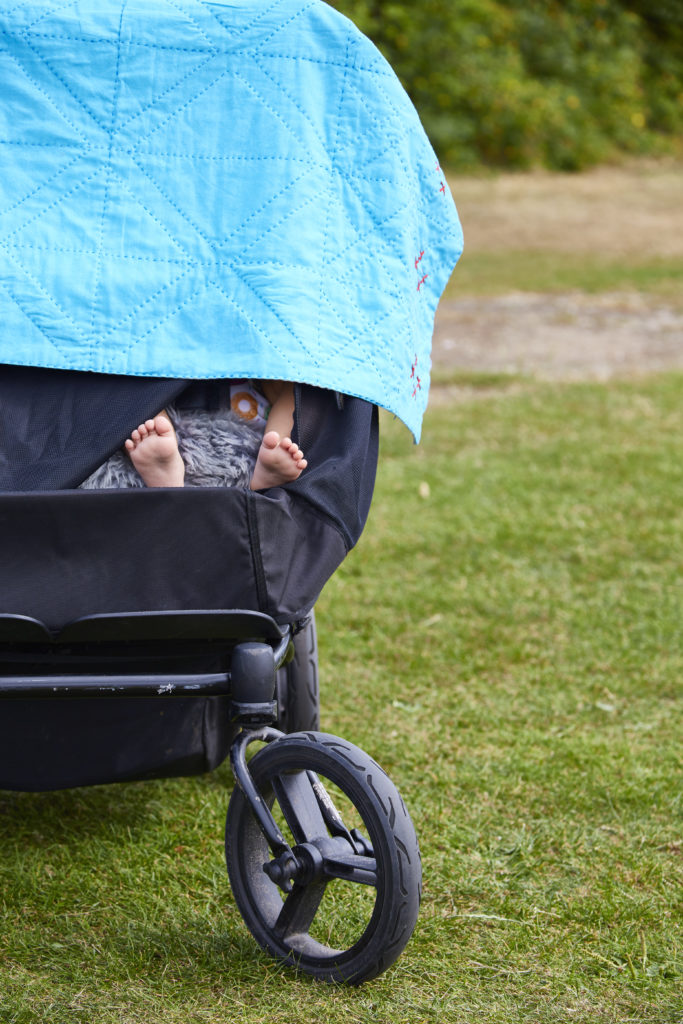 A baby in a pram outdoors with a Khushi Kantha blanket over the top shielding their eyes