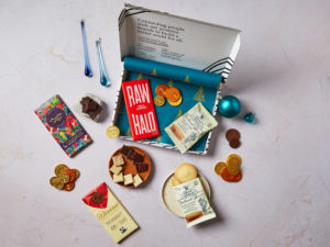 The Chocolate Letterbox Gift by Social Supermarket – the box lid is open showing the Christmas tree tissue paper and its contents are scattered, including chocolate bars from Raw Halo, Divine Chocolate and Chocolate and Love, plus Island Bakery biscuit packs.