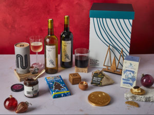 The Christmas Chill Gift Box surrounded by the contents that are inside, including two bottles of Sea Change wine, Tony's Chocolonely 51% Dark Chocolate Candy Cane, Island Bakery Black Pepper Oatcakes, Rubies in the Rubble Chilli Onion Relish and more.