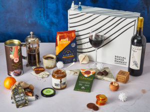 The Clementine & Clove Gift Box surrounded by the contents that are inside, including Sea Change wine, Cafédirect coffee, Divine Chocolate, Rubies in the Rubble relish, Spice Kitchen Mulled Spice Kit and more.