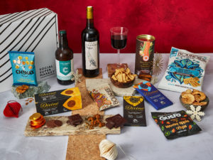 The Merry & Bright Gift Box surrounded by the contents that are inside, including Sea Change Wine, Boundless Activated Snacking crisps, Divine Chocolate bars and Ginger Thins, Crumbs Brewing beer and more.