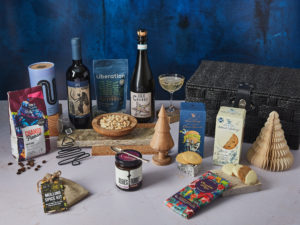 The Night Before Christmas Hamper surrounded by the contents that are inside, including Sea Change Prosecco and San Patrignano wine, Island Bakery biscuits NEMI Teas tea, Change Please coffee and more. 