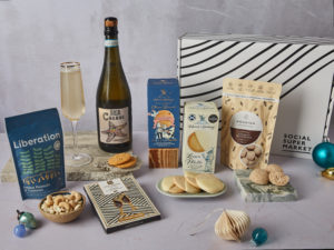 The Sparkling Celebration Gift Box surrounded by the contents that are inside, including Sea Change Prosecco, Island Bakery sweet and savoury biscuits, Nourish macaroons, Love Cocoa Prosecco chocolate and more.