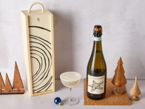 a bottle of Sea Change Prosecco next to a coup glass and the wooden wine box it comes in, surrounded by Christmas tree decorations