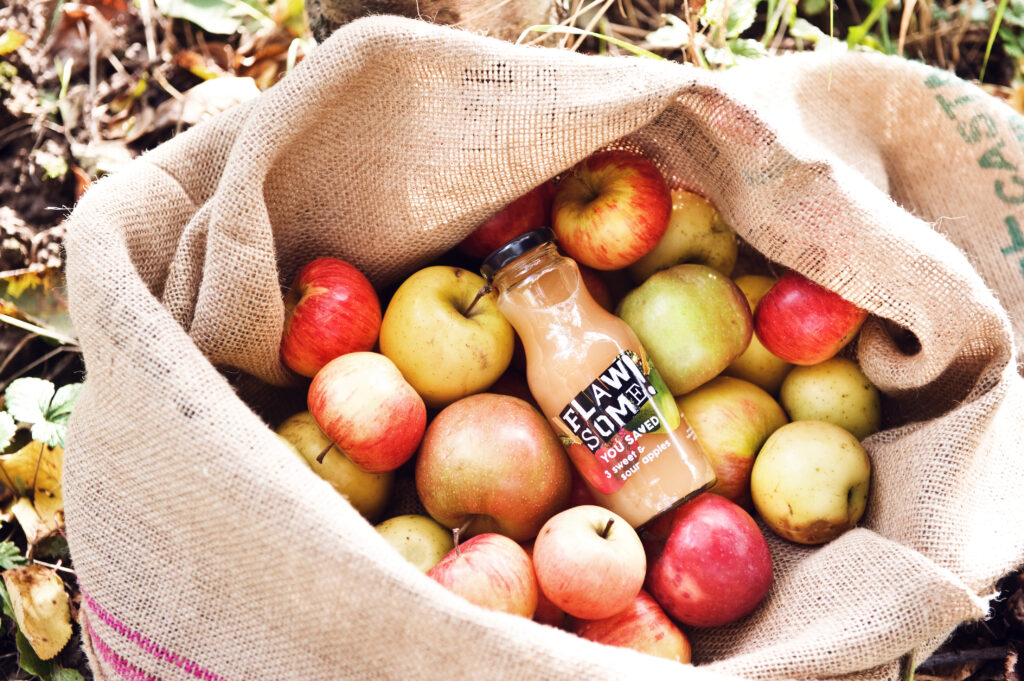 A hessian sack of apples with a bottle of Flawsome! apple juice on top