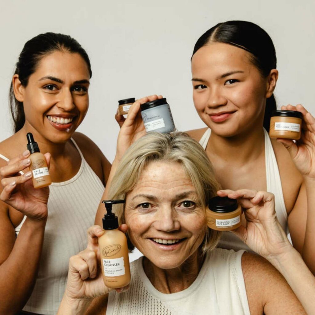 Three women hold up UpCircle beauty products while smiling